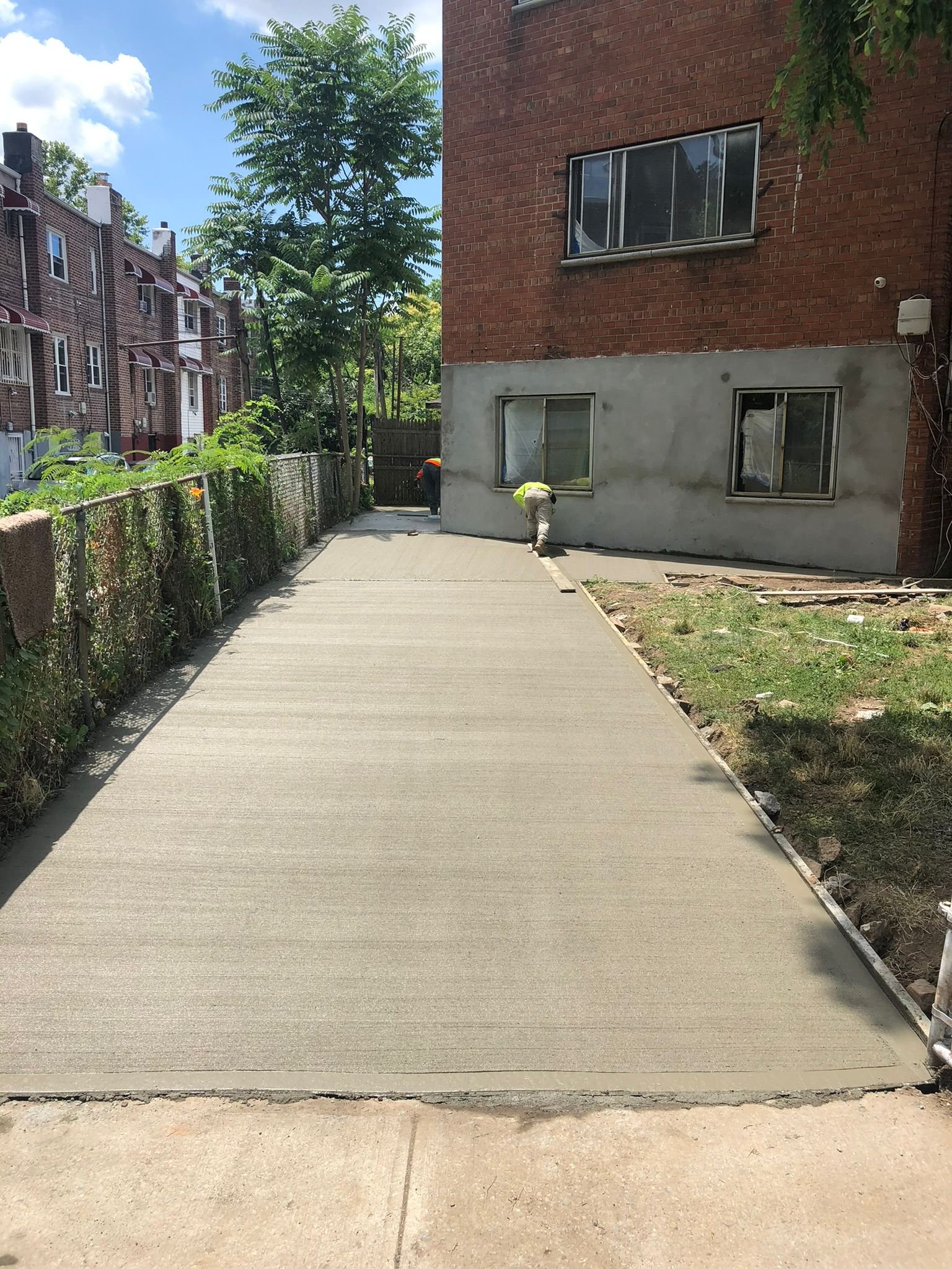 Workers repairing and leveling a concrete sidewalk beside a residential building in the Bronx.