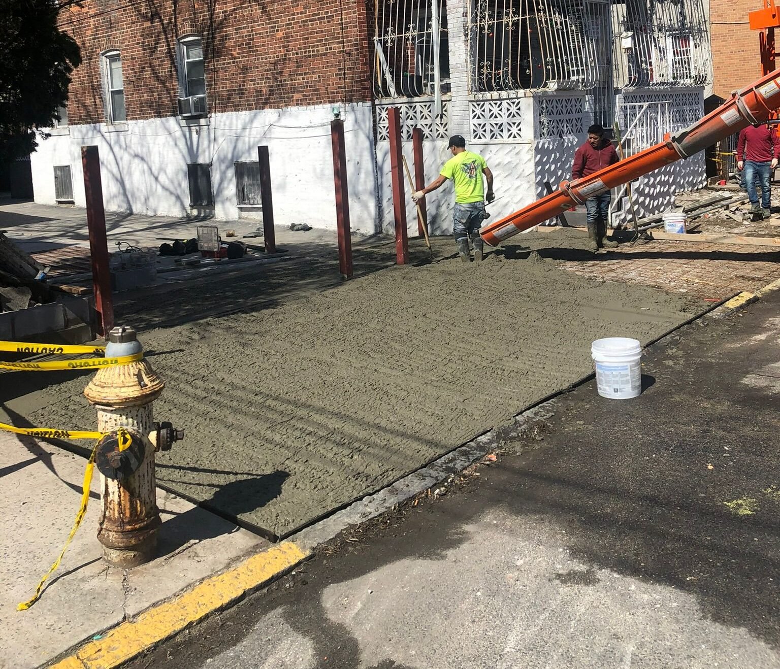 Workers pouring and leveling fresh concrete on a residential sidewalk during construction in NYC.