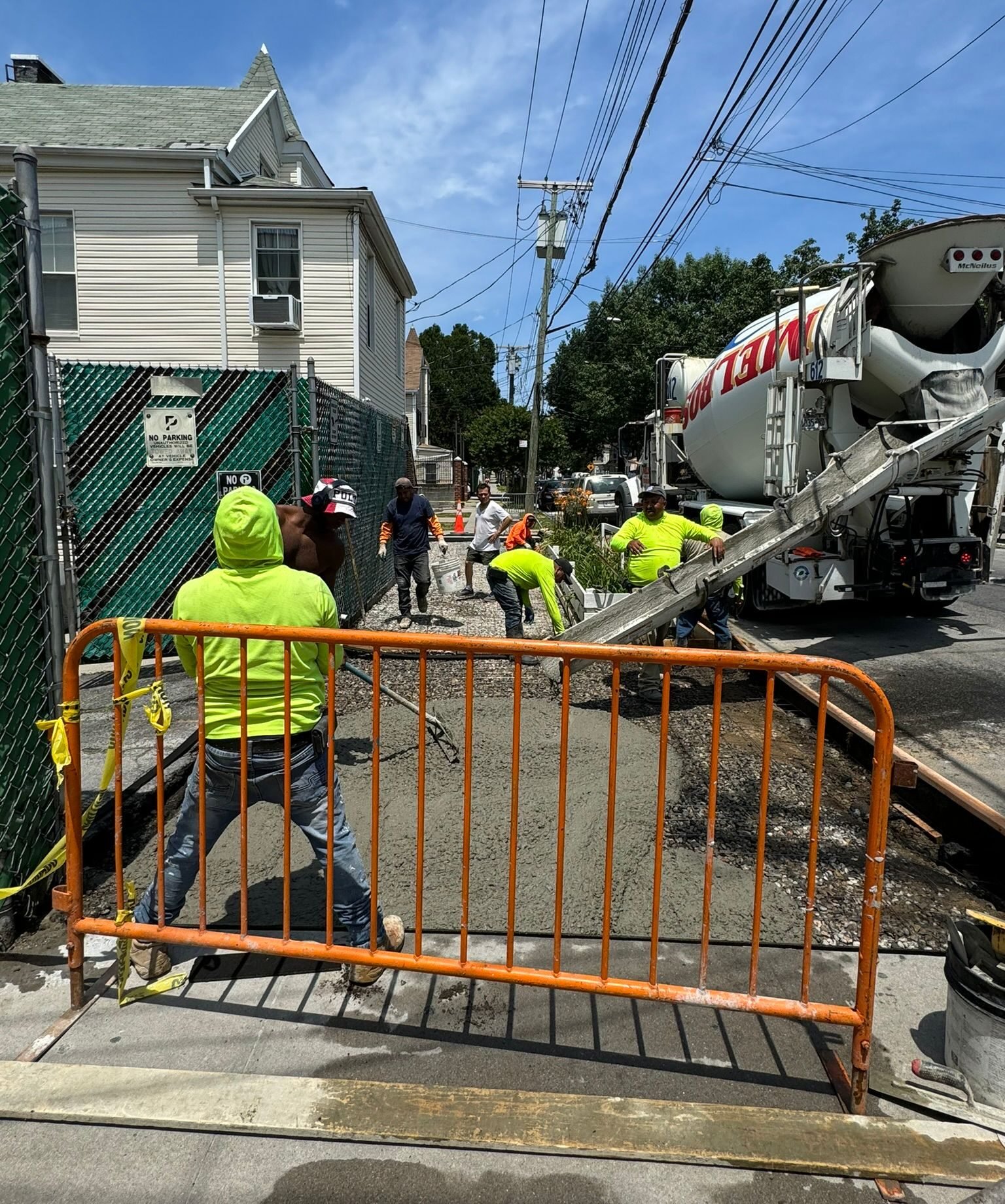 Concrete crew working beside a residential home with a cement truck pouring concrete on a sunny day in NYC.